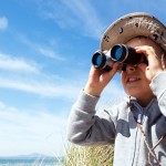 Little boy searching with binoculars at the beach dressed as explorer concept for nature, discovery, exploring and education